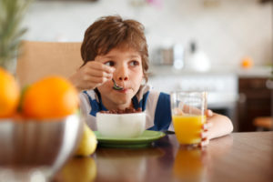 Bambino fa colazione con latte, cereali e succo di frutta