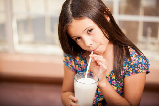 latte, bambina che beve latte dal bicchiere con la cannuccia
