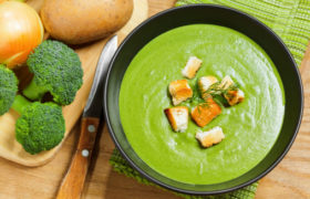 Vellutata di verdure con crostini, accanto a broccoli, patate e coltello