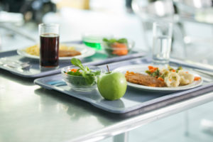 Vassoi con piatti di carne e verdure, frutta e insalata, acqua e bibita sul tavolo di una mensa