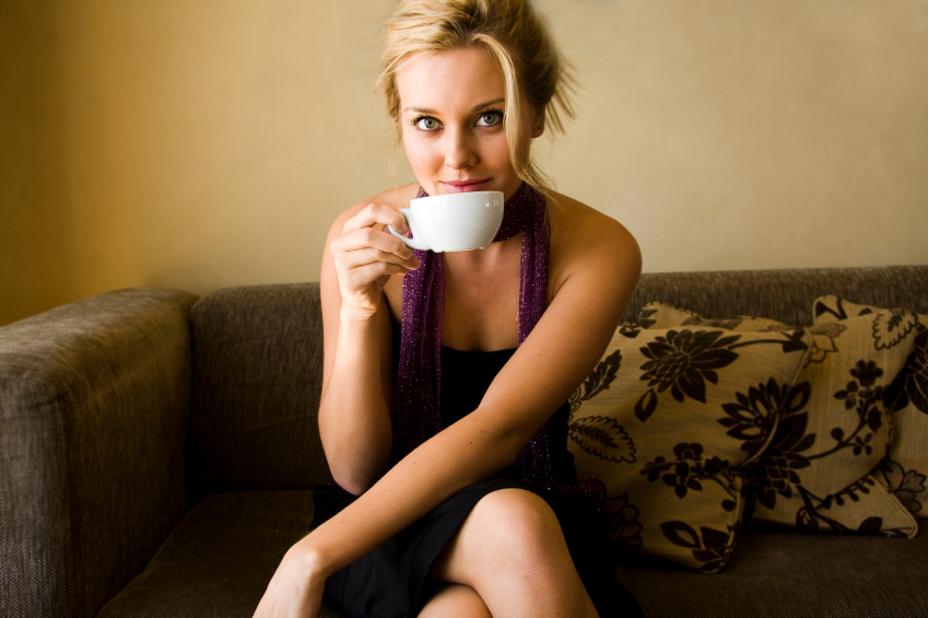 donna che beve caffè da una tazzina bianca seduta sul divano