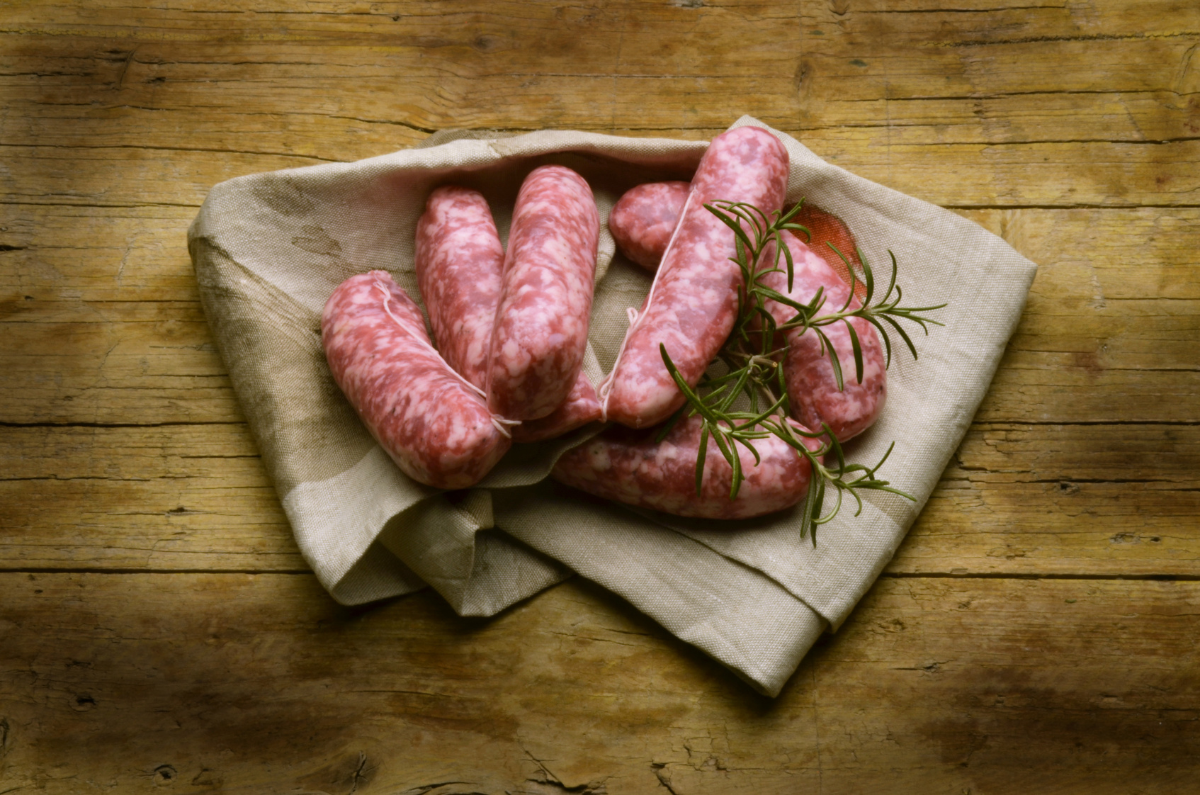 Filza di salsicce fresche con rametti di rosmarino su un panno; concept: salsiccia