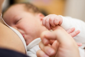 Donna allatta al seno un neonato tenendo la manina con un dito