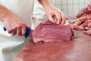 Macellaio taglia fettina di carne bovina con coltello; concept: macello, macelleria