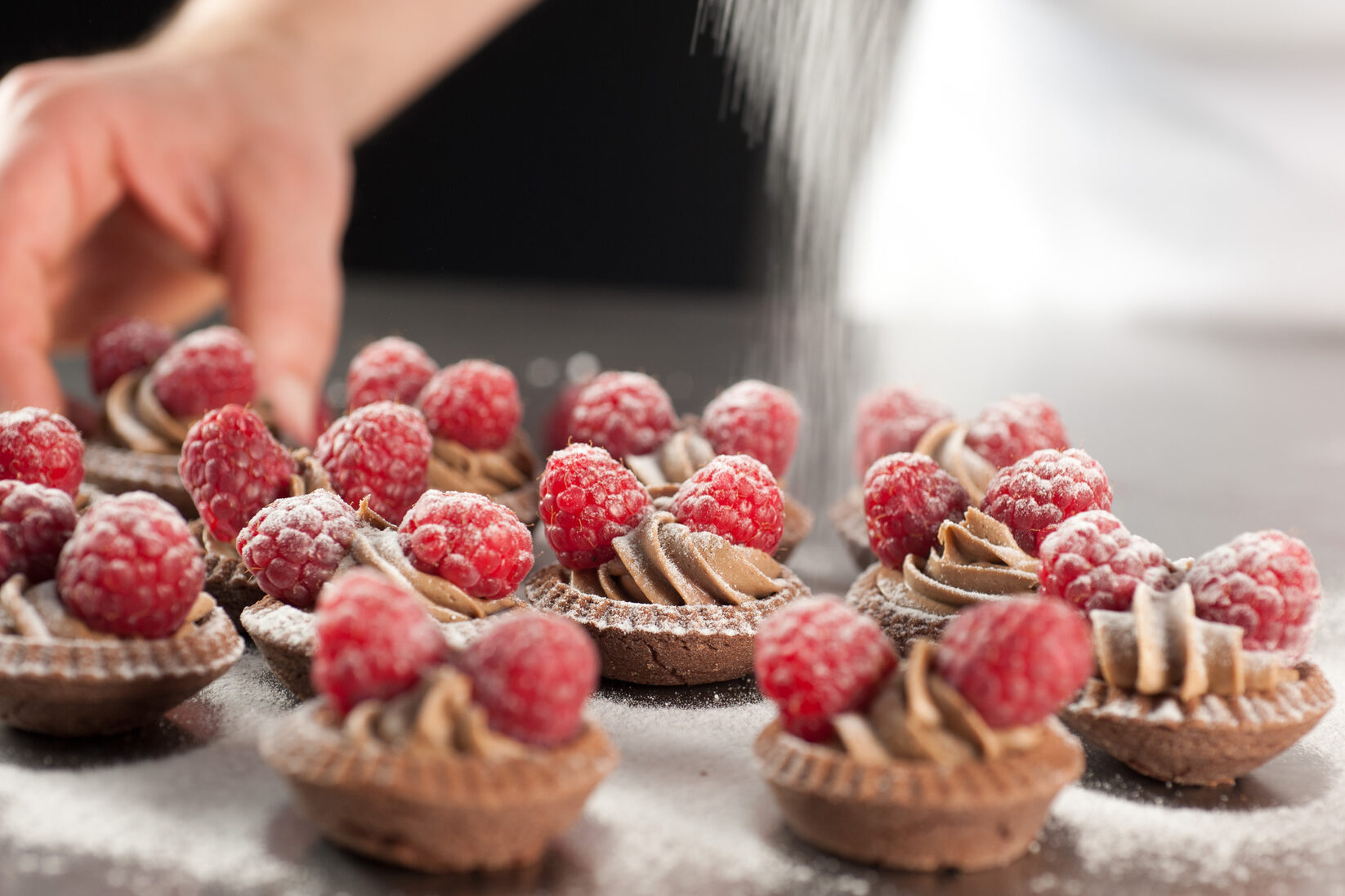 Pasticcini di frolla con crema al cioccolato e lamponi, preparati in pasticceria da un pasticcere; concept: dolci