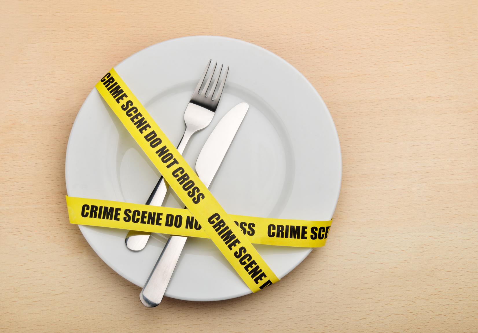 Piatto con forchetta e coltello avvolti da nastro giallo con scritta “crime scene do not cross”; concept di allerte alimentari