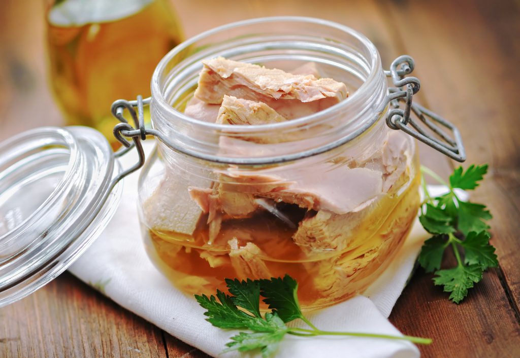 Tuna with parsley in a glass jar on wooden table
