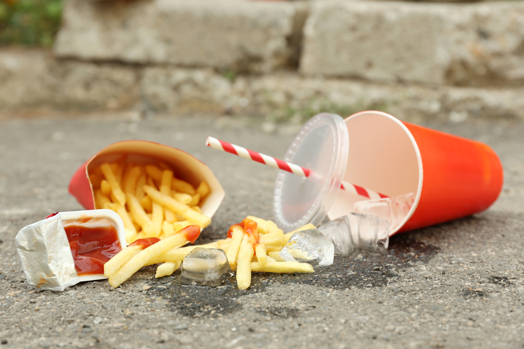 Patatine fritte, ketchup e bibita con ghiaccio di un fast food rovesciate a terra sull'asfalto; concept: junk food, linee guida nutrizionali