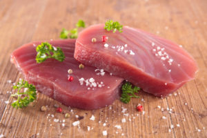 Filetti di tonno crudi con cristalli di sale, grani di pepe e prezzemolo su un tavolo di legno