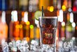 Bicchiere di bevanda tipo cola sul bancone di un bar, con cubetti di ghiaccio sparsi