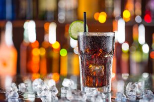 Bicchiere di bevanda tipo cola sul bancone di un bar, con cubetti di ghiaccio sparsi