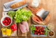 Alimenti di una dieta sana: pagnotta, latte, tranci di salmone, insalata, fette di petto di pollo, peperoni, broccoli ravanelli