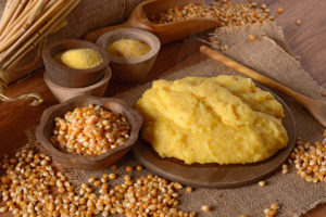 Polenta su un piatto di legno accanto a chicchi di mais e farina di mais