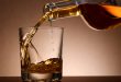 Bicchiere e bottiglia in atto versare whisky di malto, concept: alcol