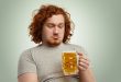 Uomo in sovrappeso guarda con espressione imbronciata un boccale di birra