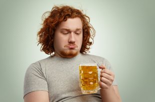 Uomo in sovrappeso guarda con espressione imbronciata un boccale di birra