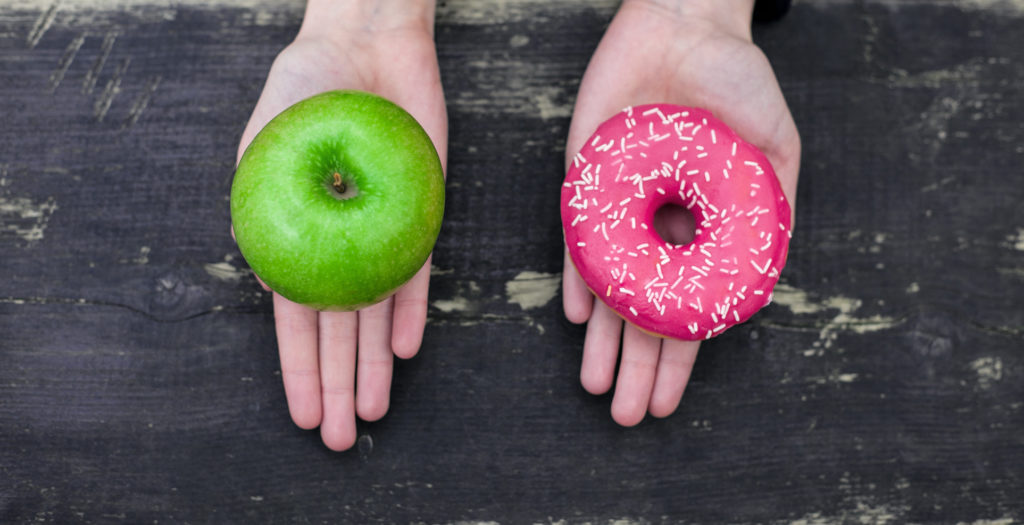 A sinistra mano con mela verde, a destra mano con ciambella glassata di rosa; concept: junk food, dieta sana