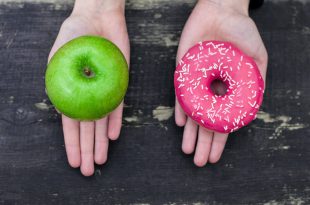 A sinistra mano con mela verde, a destra mano con ciambella con glassa rosa e zuccherini