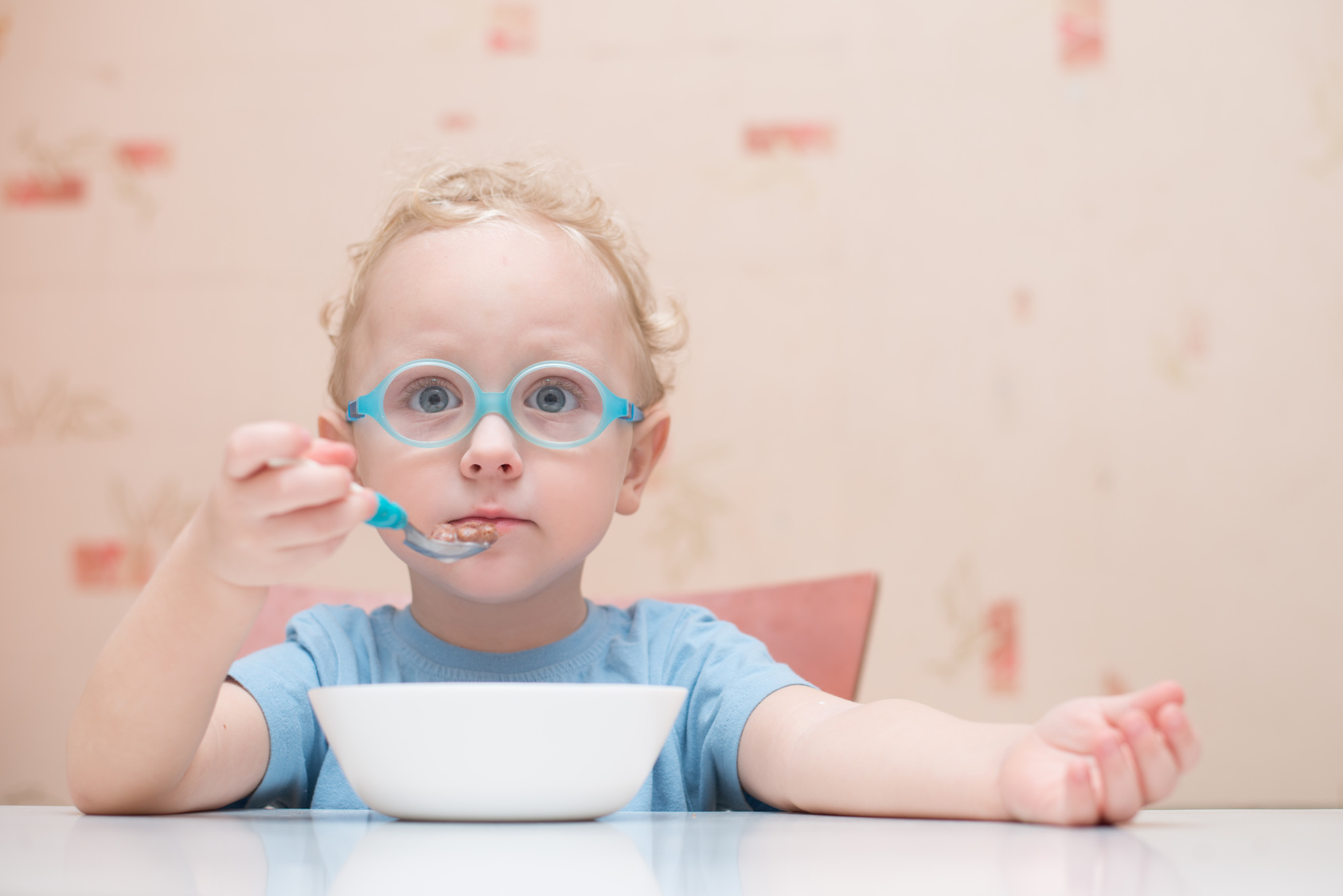 Bambino piccolo con occhiali mangia seduto a un tavolo