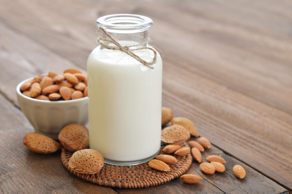 Almond milk in bottle with nuts on wooden background