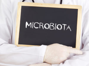 Persona con camice e guanti tiene in mano lavagnetta con la scritta microbiota