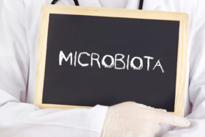 Persona con camice e guanti tiene in mano lavagnetta con la scritta microbiota