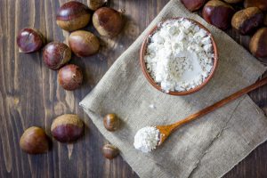 Farina di castagne in una ciotola di legno, accanto un cucchiaio di legno, intorno castagne sparse; concept: aflatossine