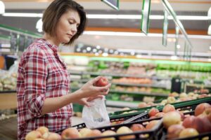 Donna sceglie mele da insacchettare nel reparto ortofrutta di un supermercato; concept: sacchetti ortofrutta, frutta e verdura