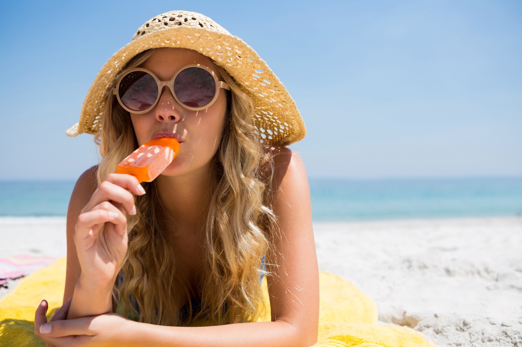 Una donna mangia un gelato o sorbetto su stecco o un ghiacciolo in spiaggia