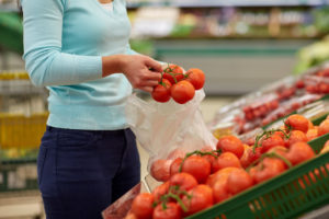 Donna mette grappolo di pomodori in un sacchetto nel reparto ortofrutta del supermercato