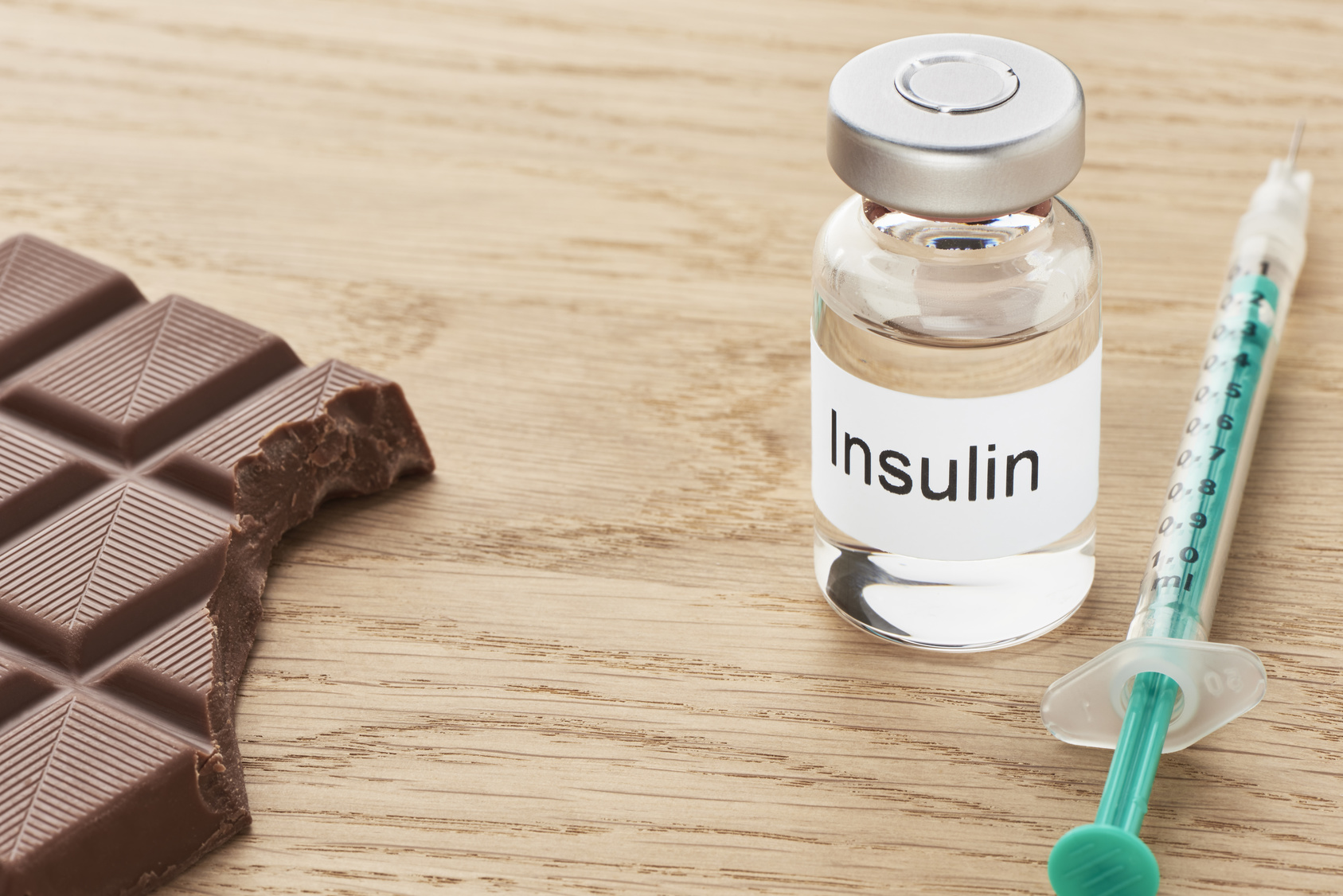 Eine Insulinampulle steht zusammen mit einer Spritze auf einem Tisch daneben liegt ein angebissenes stück Schokolade.