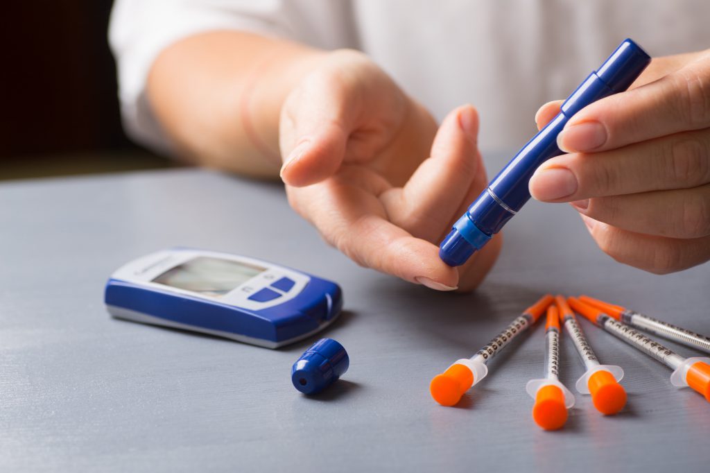 Persona diabetica misura la glicemia, con siringhe di insulina sul tavolo; concept: diabete