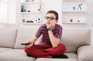 Ragazzo adolescente annoiato sul divano con in mano il telecomando della televisione