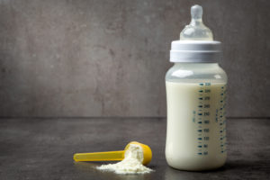 Biberon con latte accanto a misurino con latte in polvere; concept: latte crescita, formula