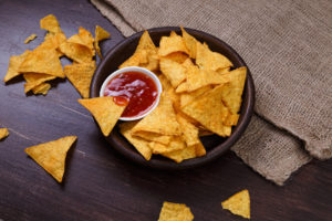 Tortilla o nacho chips in un piattino nero con ciotola di salsa