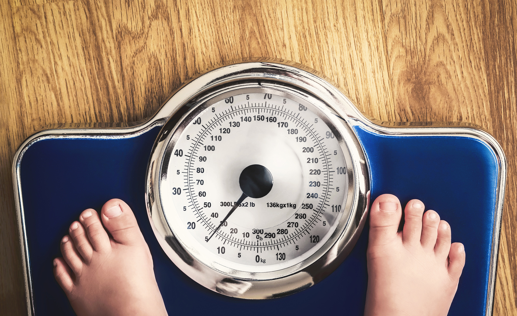 Piedi di bambino su bilancia analogica blu; concept: obesità, sovrappeso
