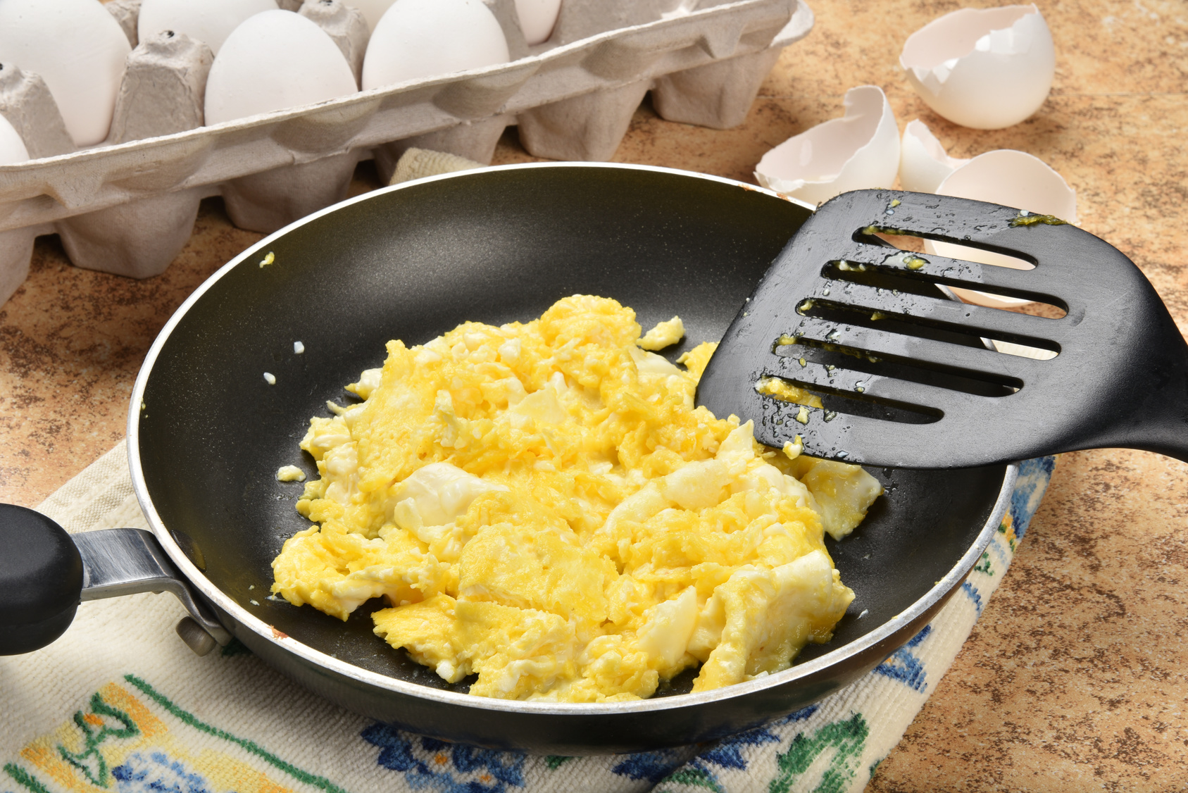 Uova strapazzate in padella antiaderente con paletta accanto a cartone delle uova