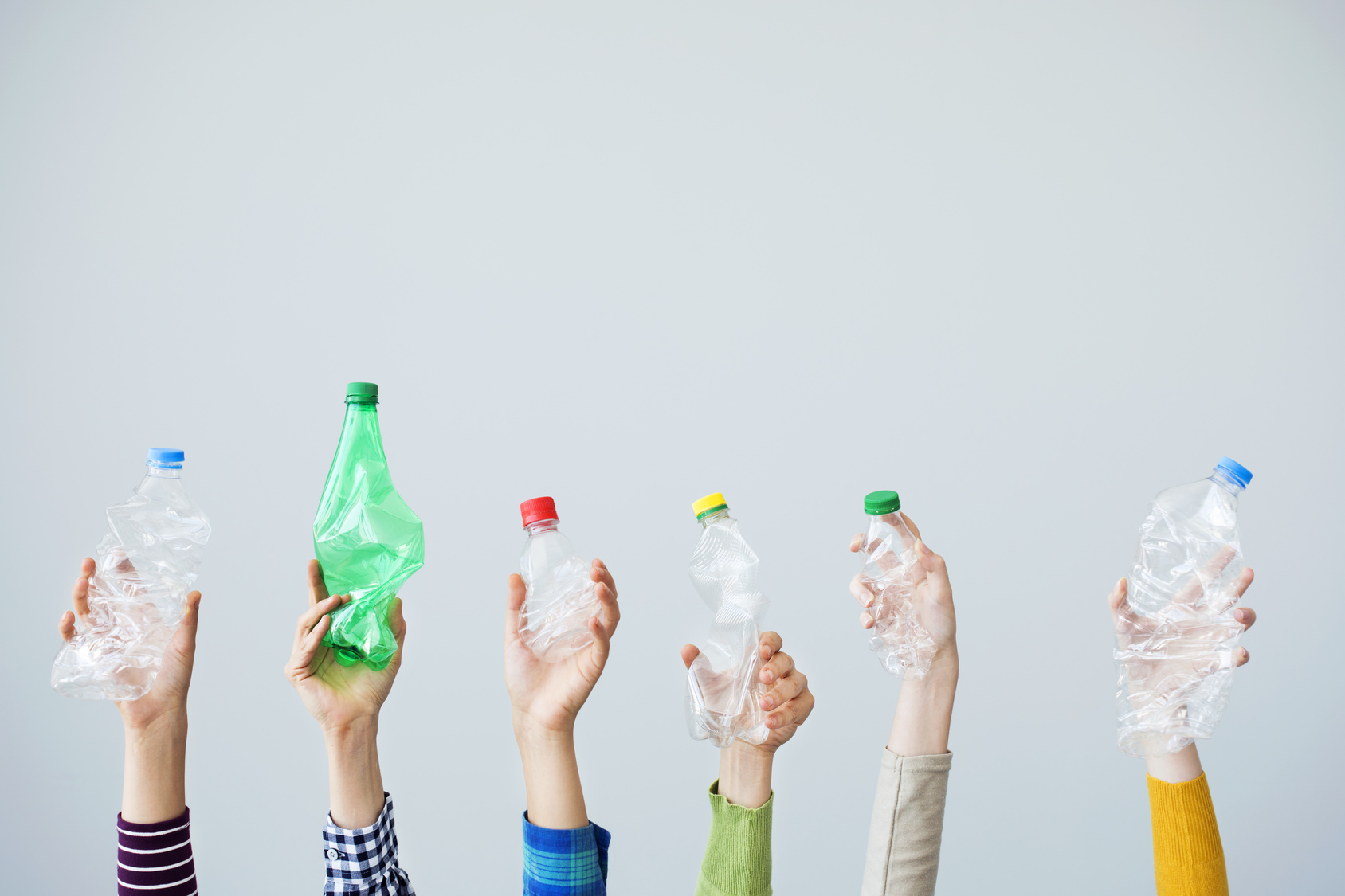 Mani che tengono bottiglie di plastica schiacciate su sfondo bianco; concept: riciclo, raccolta differenziata, vuoto a rendere, deposito cauzionale
