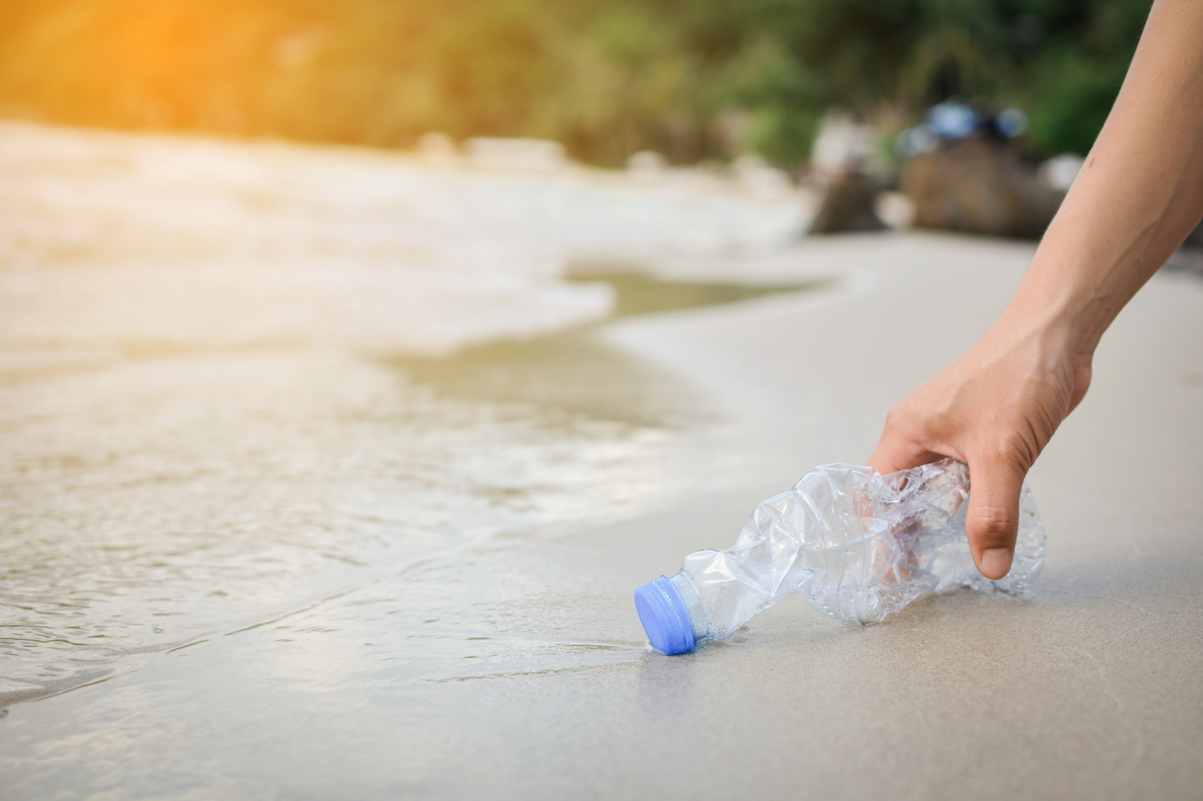 Mano femminile raccoglie bottiglia di plastica su una spiaggia
