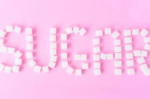 Sugar text with sugar cubes on sweet pink background, food and healthy concept