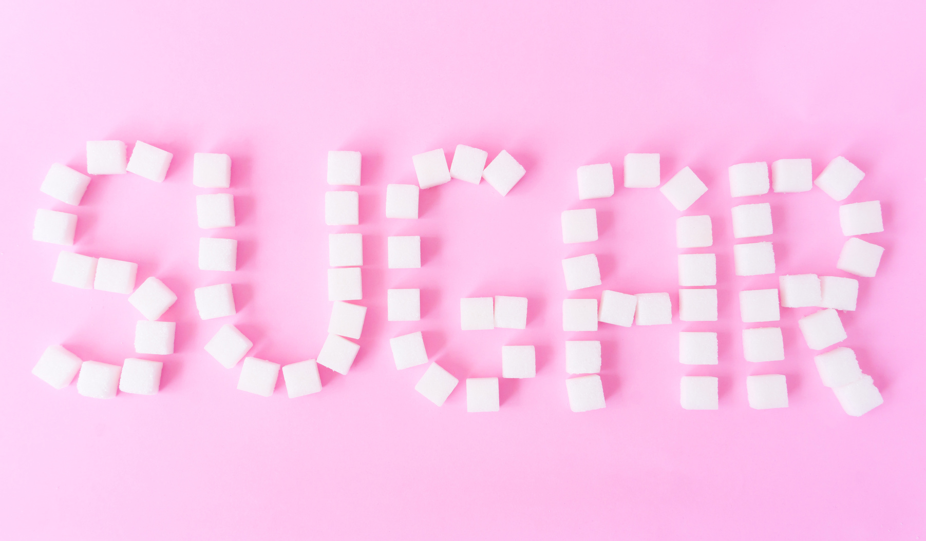 Sugar text with sugar cubes on sweet pink background, food and healthy concept