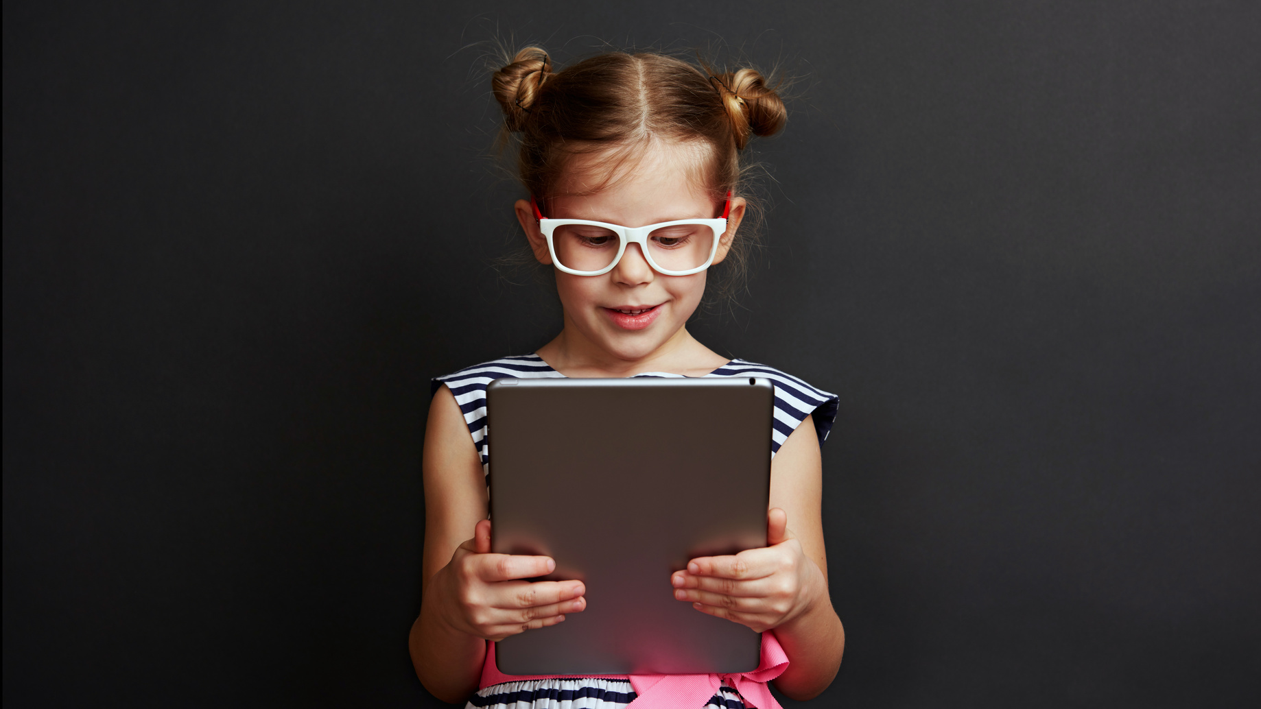 Adorable girl playing game on digital tablet over dark background. Technology and lifestyle.