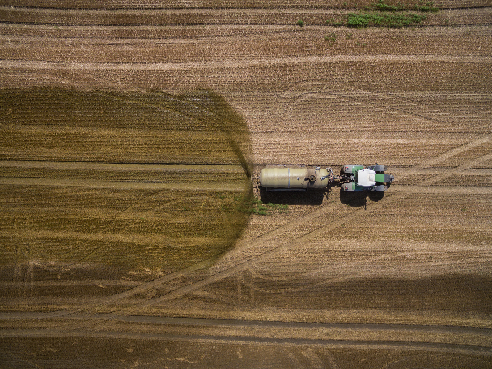 aerial view of a tractor with a trailer fertilizes a freshly plowed agriculural field with manure in germany