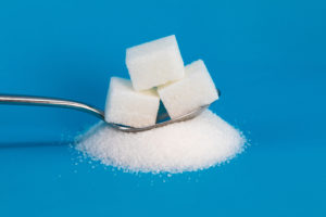 Tre zollette di zucchero su un cucchiaino appoggiato su un mucchietto di zucchero