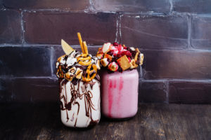 Due milkshake con bretzel, pop corn, marshmallows e altro; concept: junk food, ultraprocessati, ultra-trasformati, freakshake