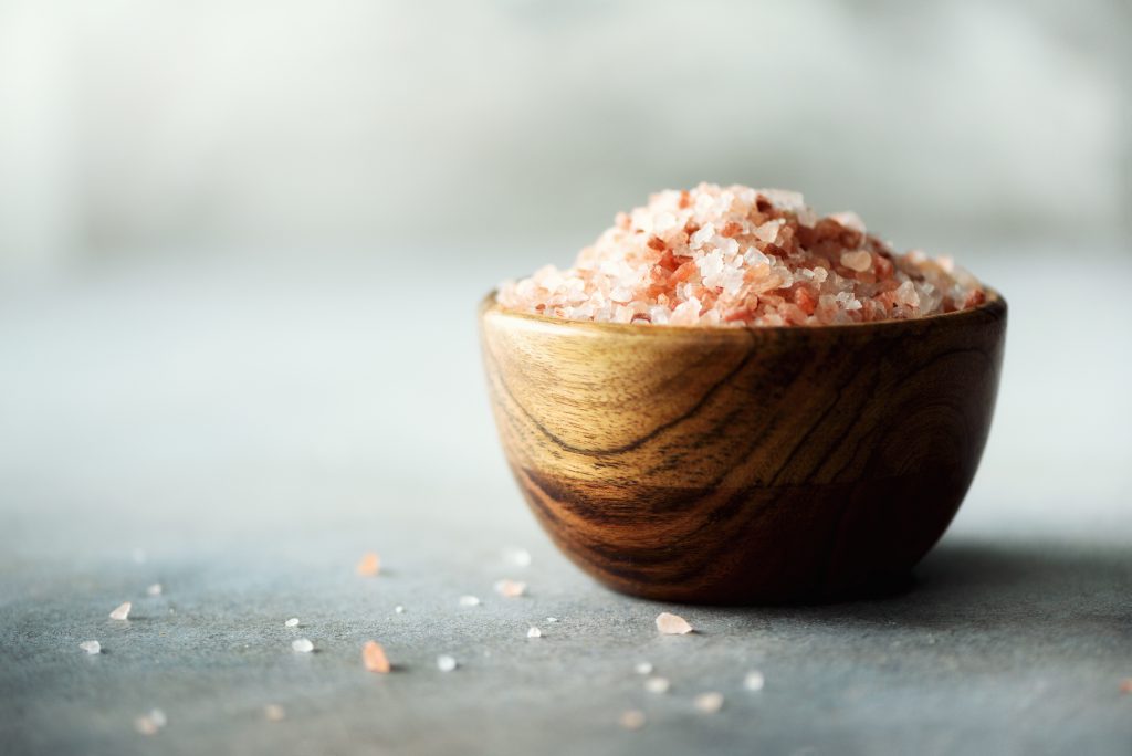 Pink Himalayan salt crystals and powder in wooden bowls on grey concrete background. Healthy diet without salt. Copy space