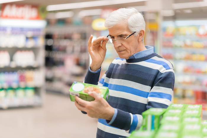 Uomo anziano con gli occhiali legge l'etichetta di un prodotto al supermercato