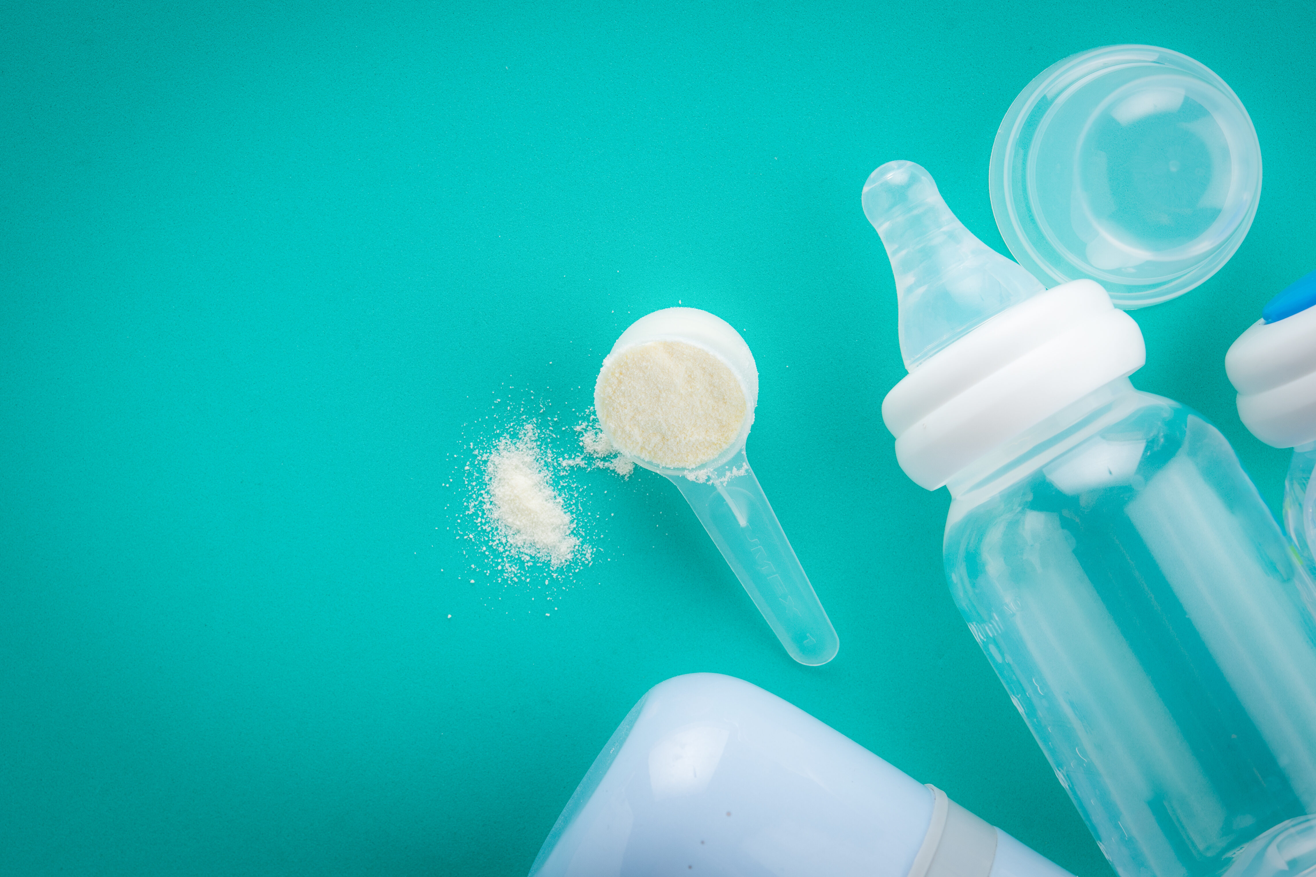 Misurino di latte in polvere, con biberon trasparente su sfondo verde-azzurro
