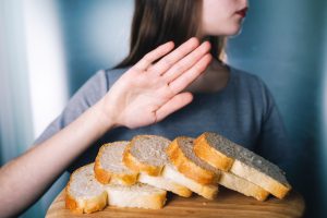 Donna fa gesto di rifiuto davanti a fette di pane su un tagliere; concept: celiachia, intolleranza al glutine