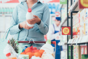 Donna con carrello della spesa legge etichetta di una bottiglia di latte al supermercato